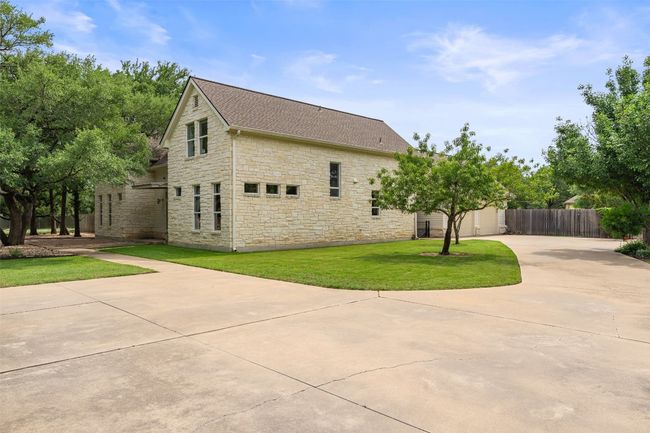 View of property exterior with stone siding, a shingled roof, and concrete driveway | Image 10