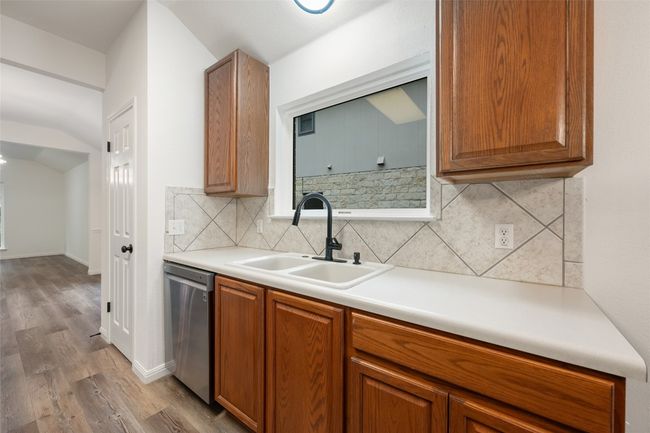 Kitchen featuring stainless steel dishwasher, wood finished floors, backsplash, brown cabinetry, and lofted ceiling | Image 21