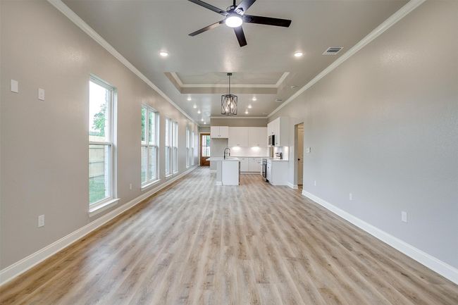Unfurnished living room with crown molding, baseboards, light wood finished floors, and visible vents | Image 7
