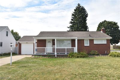 Ranch-style house featuring a garage, a front lawn, and a porch | Image 1