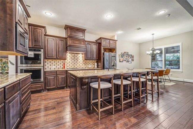 Gourmet kitchen features rich wood cabinetry, granite countertops, a large island with bar seating, and an open layout that flows into a bright breakfast area. | Image 16