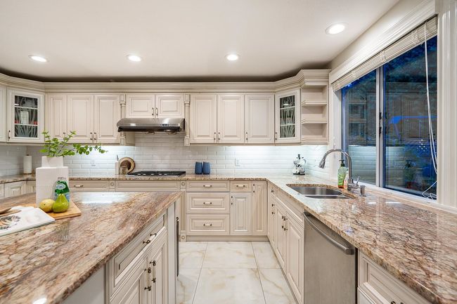 Kitchen with stainless steel appliances, a sink, under cabinet range hood, backsplash, and glass insert cabinets | Image 11