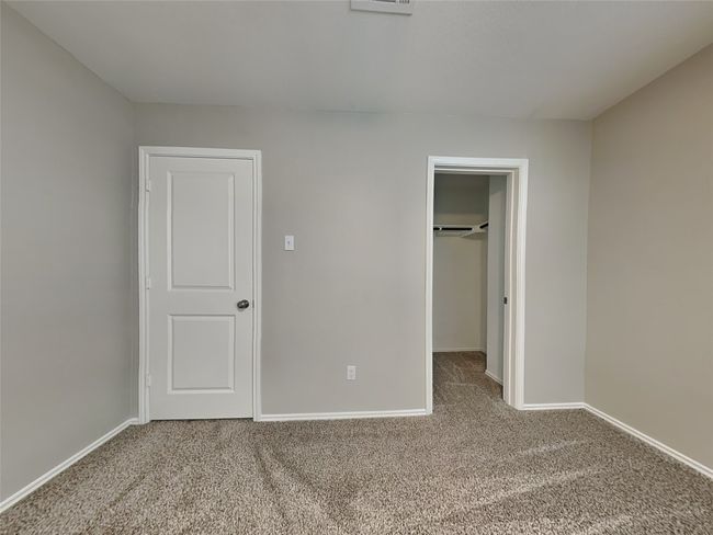 Unfurnished bedroom with carpet flooring, a walk in closet, baseboards, and a closet | Image 5
