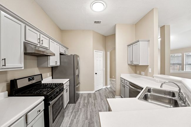 Kitchen featuring stainless steel appliances, light countertops, light wood finished floors, under cabinet range hood, and a peninsula | Image 10