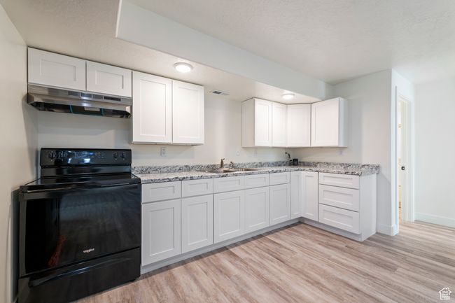 Kitchen featuring light wood-type flooring, black range with electric stovetop, under cabinet range hood, and a sink | Image 34