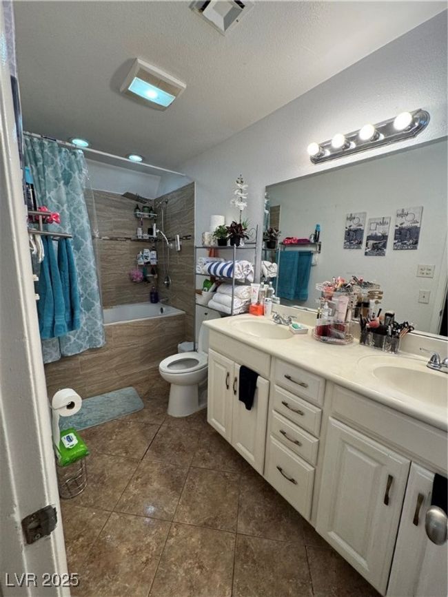 Full bath featuring tiled shower / bath combo, double vanity, tile patterned floors, and toilet | Image 12