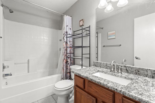Full bathroom featuring shower / bath combo, vanity, toilet, a textured ceiling, and tile patterned flooring | Image 25