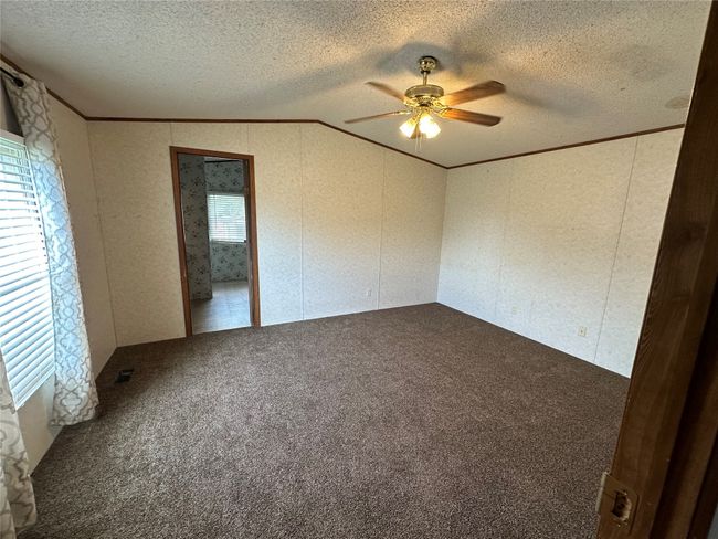 Carpeted empty room with ceiling fan, a textured ceiling, crown molding, and a decorative wall | Image 17