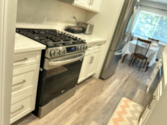 Kitchen with stainless steel gas stove, light countertops, white cabinets, and light wood-style floors | Image 7
