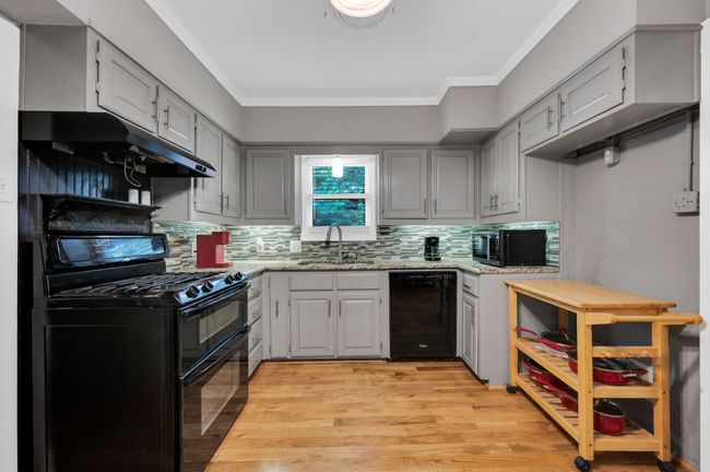 Kitchen with black appliances, under cabinet range hood, a sink, light wood-style floors, and backsplash | Image 10