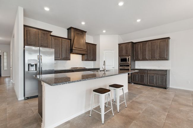 Kitchen featuring appliances with stainless steel finishes, custom exhaust hood, decorative backsplash, dark stone counters, and dark brown cabinetry | Image 8