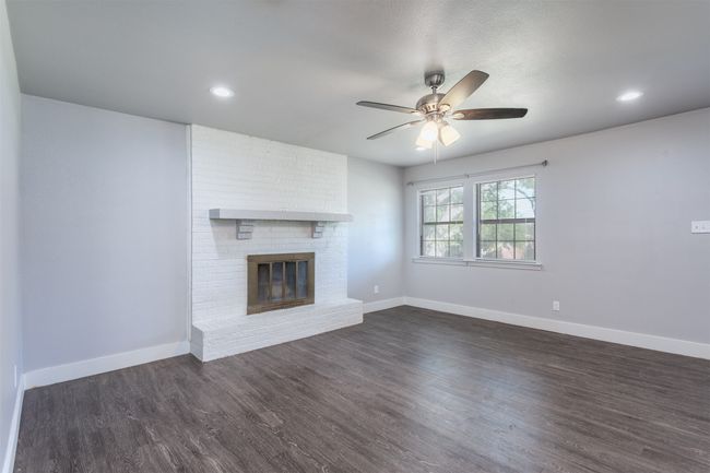 Unfurnished living room with baseboards, a brick fireplace, a ceiling fan, and dark wood-style floors | Image 4