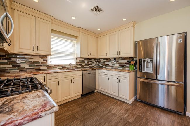 Kitchen featuring cream cabinetry, appliances with stainless steel finishes, decorative backsplash, and visible vents | Image 5