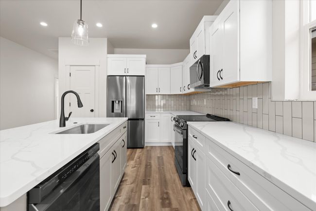 Kitchen with tasteful backsplash, light wood-type flooring, white cabinets, black appliances, and a sink | Image 8