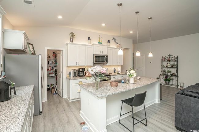 Kitchen featuring stainless steel appliances, light wood-style floors, a breakfast bar area, white cabinetry, and light stone counters | Image 19