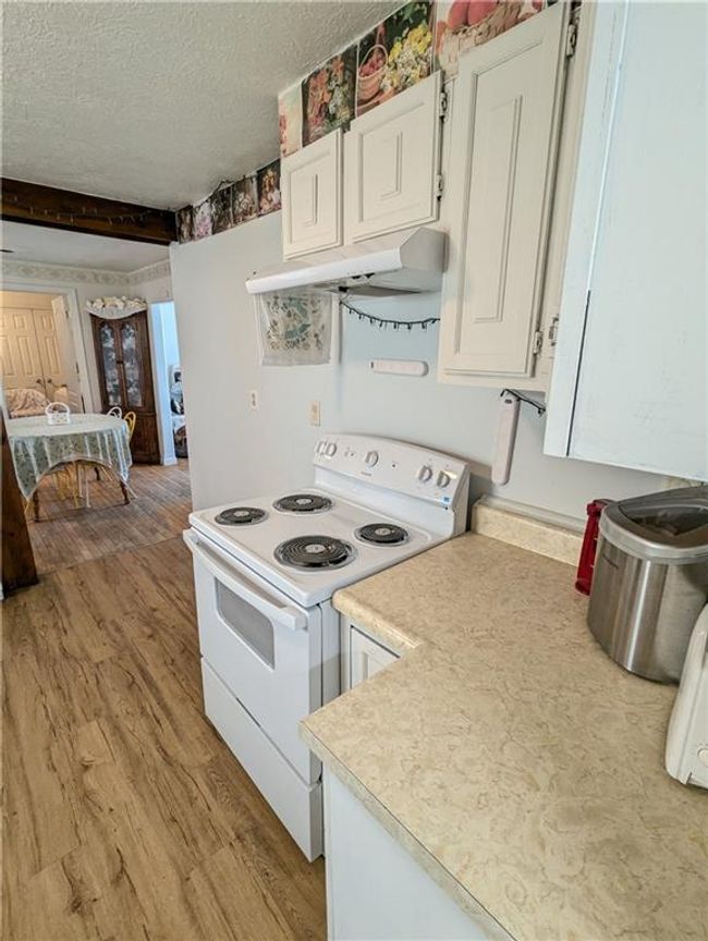 Kitchen with white electric stove, under cabinet range hood, white cabinetry, and light wood-type flooring | Image 14