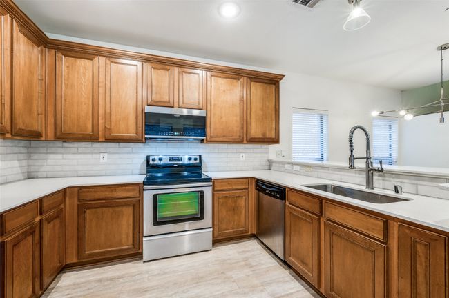 Kitchen featuring appliances with stainless steel finishes, brown cabinets, backsplash, light countertops, and pendant lighting | Image 11