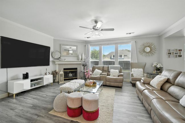 Living area featuring a ceiling fan, crown molding, wood finished floors, and a tiled fireplace | Image 10
