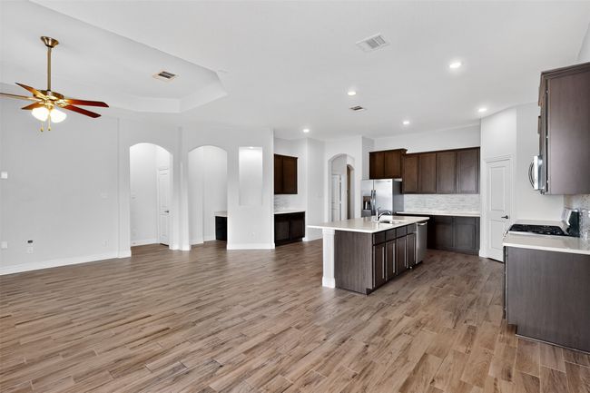Kitchen with open floor plan, arched walkways, a kitchen island with sink, appliances with stainless steel finishes, and dark brown cabinets | Image 6