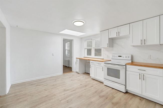 Kitchen with white cabinets, radiator, a skylight, butcher block counters, and electric stove | Image 9