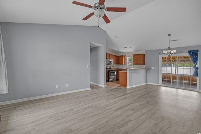 Unfurnished living room featuring vaulted ceiling, a chandelier, ceiling fan, baseboards, and light wood-type flooring | Image 12
