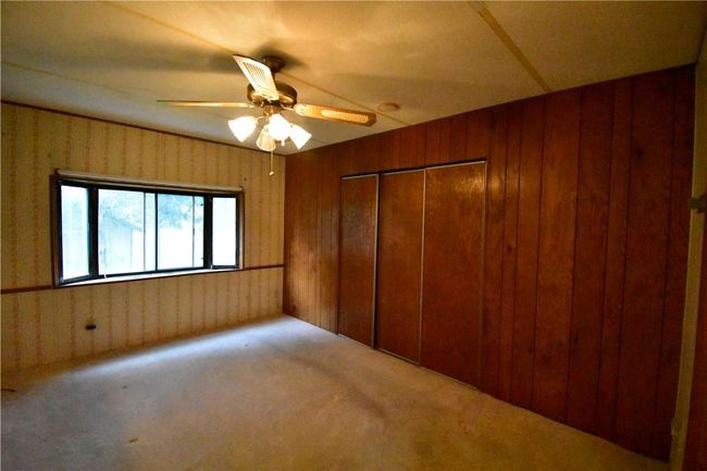 Unfurnished bedroom featuring a closet, carpet, ceiling fan, and wood walls | Image 17