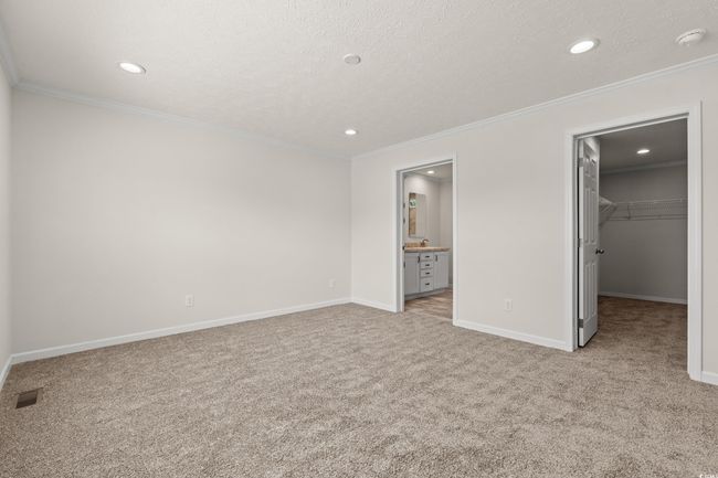 Unfurnished bedroom featuring a walk in closet, crown molding, carpet flooring, and visible vents | Image 16