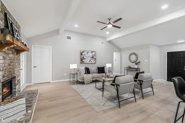 Living area featuring light wood-style flooring, a ceiling fan, a brick fireplace, visible vents, and vaulted ceiling with beams | Image 6