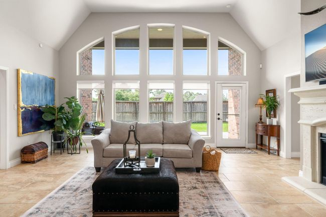 Bask in natural light in this beautifully designed living room featuring a dramatic wall of arched windows, elegant neutral tones and seamless access to the backyard through a full glass door. | Image 7