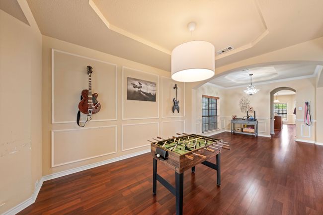 Playroom featuring visible vents, a tray ceiling, a decorative wall, dark wood finished floors, and arched walkways | Image 16