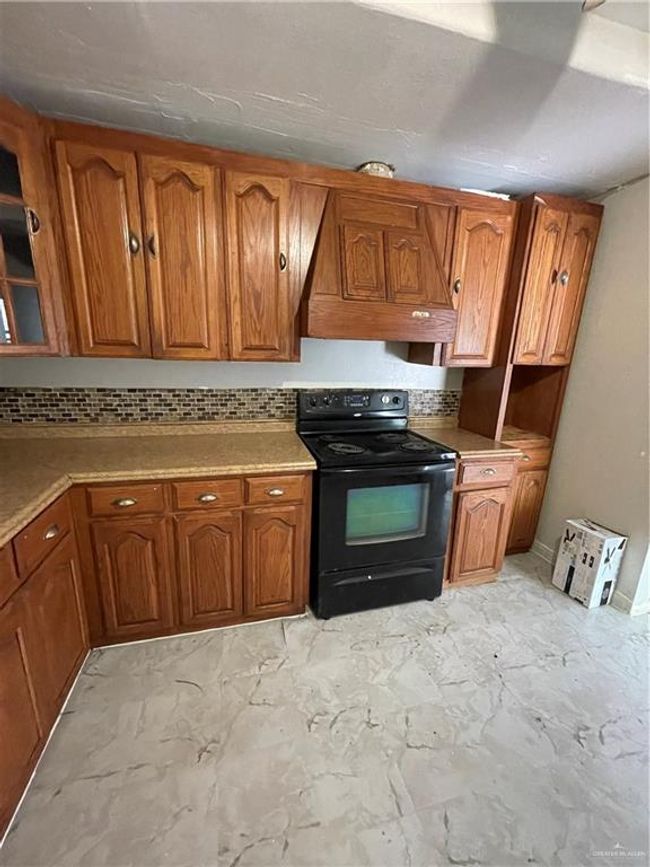 Kitchen featuring electric range, brown cabinets, backsplash, light marble finish flooring, and light countertops | Image 8