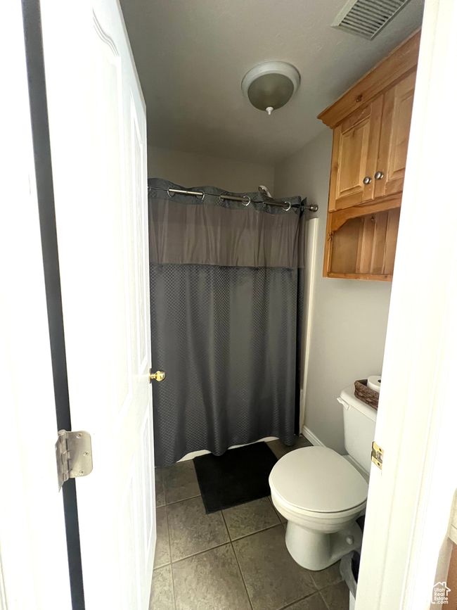 Bathroom with tile patterned flooring, curtained shower, toilet, and visible vents | Image 12