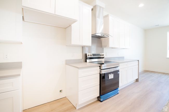 Kitchen with stainless steel range with electric stovetop, wall chimney exhaust hood, light wood-style flooring, light countertops, and white cabinetry | Image 6