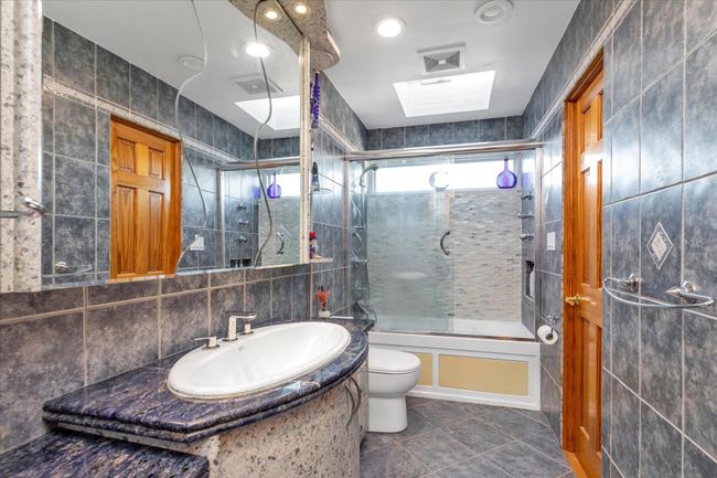 Bathroom featuring vanity, a combined bath / shower with rainfall shower, tile walls, and toilet | Image 9