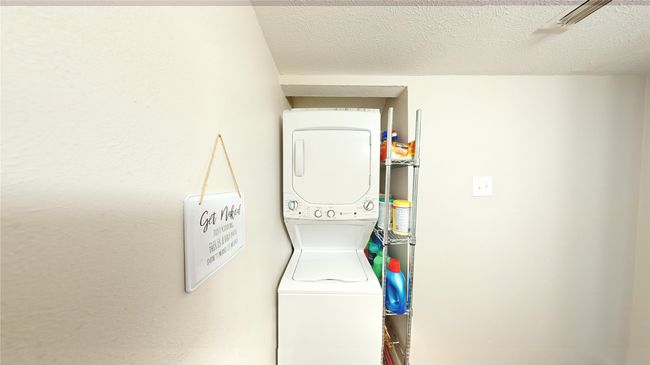 Clothes washing area with stacked washing maching and dryer, laundry area, and a textured ceiling | Image 5