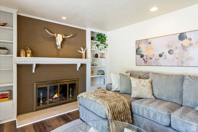 Living area featuring wood finished floors, a glass covered fireplace, recessed lighting, and built in shelves | Image 12