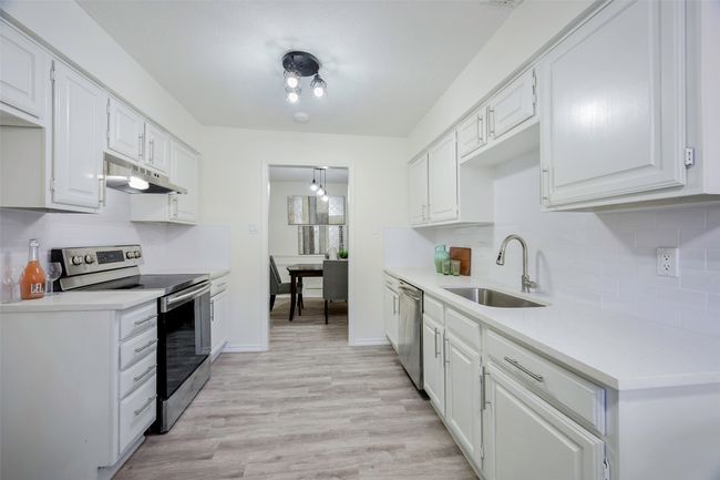 Kitchen with a sink, under cabinet range hood, stainless steel appliances, white cabinets, and decorative backsplash | Image 14