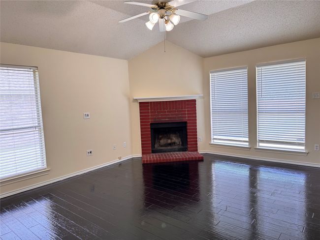Unfurnished living room featuring ceiling fan, vaulted ceiling, a textured ceiling, a brick fireplace, and wood finished floors | Image 4