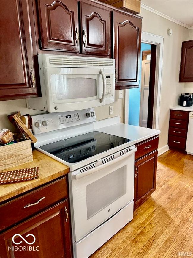 kitchen featuring white appliances, ornamental molding, light countertops, light wood-style flooring, and dark brown cabinetry | Image 21