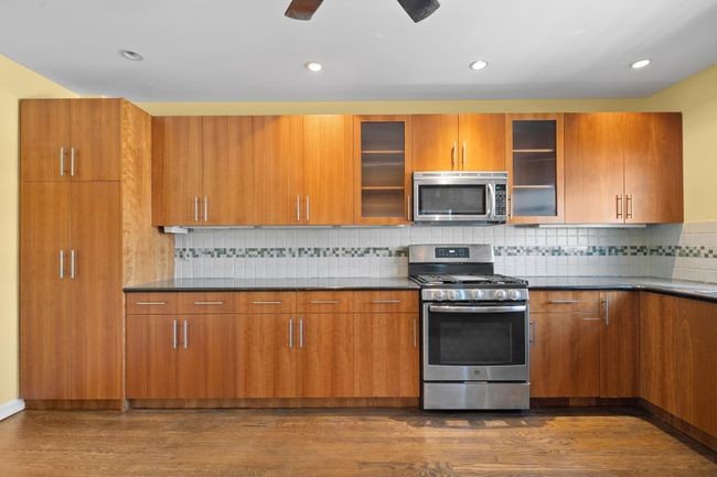 Kitchen featuring stainless steel appliances, dark wood-style floors, brown cabinetry, dark countertops, and decorative backsplash | Image 11