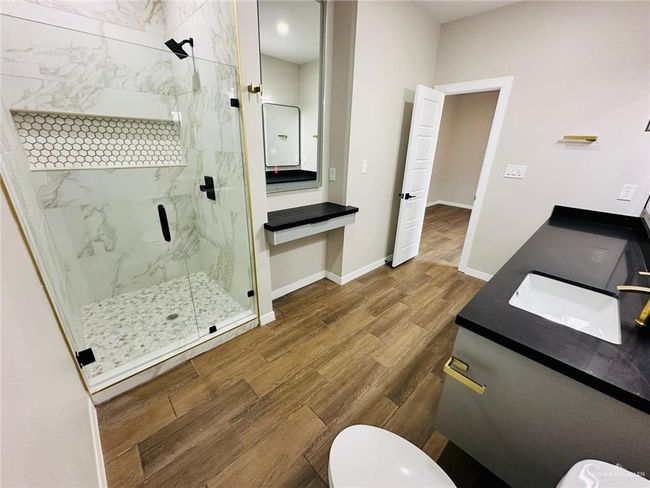 Full bath featuring a marble finish shower, wood finished floors, toilet, vanity, and baseboards | Image 9