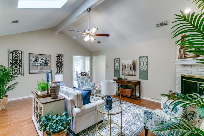 Living area with wood finished floors, a skylight, ceiling fan, and a brick fireplace | Image 6