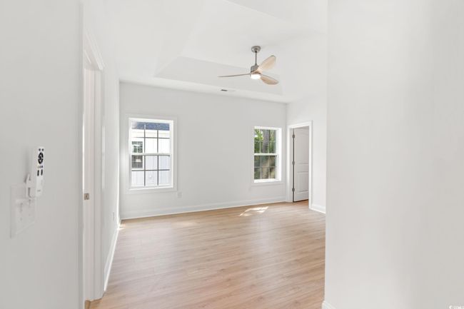 Empty room featuring light wood-style floors, a tray ceiling, and ceiling fan | Image 16