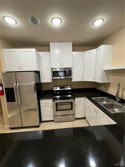 Kitchen with appliances with stainless steel finishes, sink, light tile patterned flooring, and white cabinets | Image 3