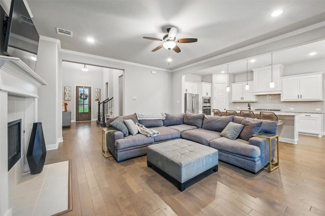 Living area featuring ceiling fan, light wood-type flooring, a tile fireplace, ornamental molding, and recessed lighting | Image 12