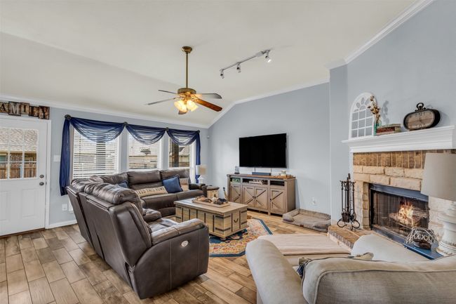Living room with a fireplace, light hardwood / wood-style flooring, crown molding, rail lighting, and ceiling fan | Image 15
