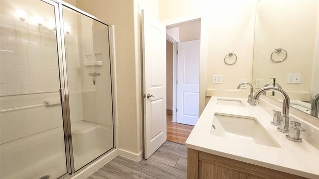Bathroom with double vanity, a sink, a stall shower, and wood finished floors | Image 6