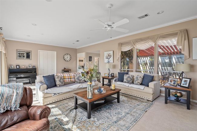 Flooded with natural light, this expansive living room offers stunning views of the lush golf course through a wall of floor-to-ceiling windows. The neutral color palette, plush carpeting, and elegant window treatments create a warm and inviting atmosphere, perfect for both relaxation and entertaining. | Image 13