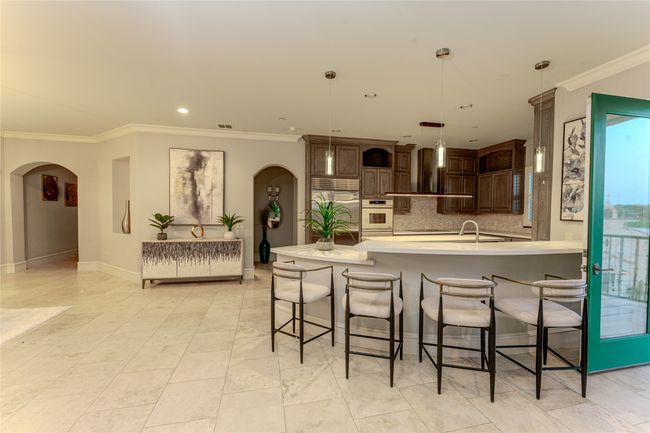 Kitchen featuring wall chimney exhaust hood, crown molding, arched walkways, built in refrigerator, and backsplash | Image 17