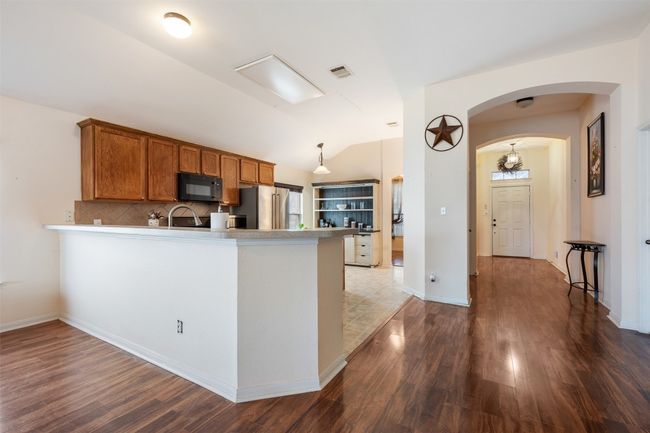 Kitchen with brown cabinets, arched walkways, vaulted ceiling, black microwave, and stainless steel fridge | Image 14